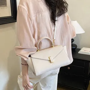 Elegant beige leather crossbody handbag with a triangular flap and gold metal clasp