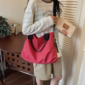 Grande borsa da viaggio a scacchi rossi portata da una modella in un contesto casual.