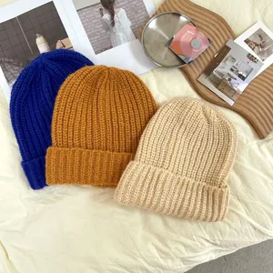 Close-up of three thick ribbed knit beanies in blue, yellow, and beige for winter