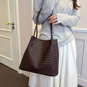 Detail view of a large brown woven tote bag carried by a model in a casual outfit.
