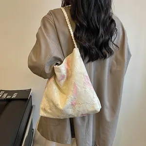 Close-up view of delicate pink floral embroidery on a cream-colored Chinese style bucket bag