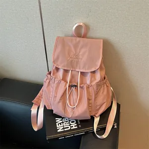 Stylish pink drawstring pleated backpack shown resting on a book in an urban setting