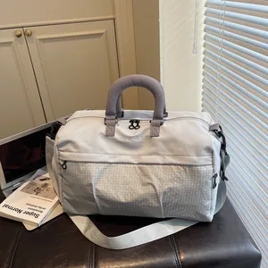 Stylish light grey travel duffel bag with grey handles on a dark leather bench.