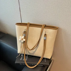 Close-up detail of a large capacity woven tote bag featuring brown straps and a flower charm