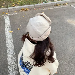 Rear view of a cream-colored plush winter hat with earflaps and warm fleece lining