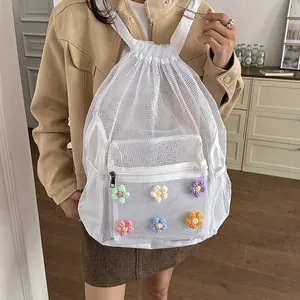 Close-up detail of a white mesh drawstring backpack featuring colorful crochet flower accents
