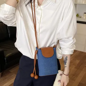 Lifestyle shot of a blue denim and brown leather crossbody phone bag for women.