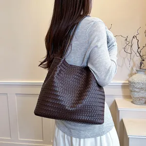 Elegant large brown woven tote bag carried as a stylish shoulder bag on a model