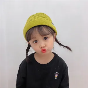 Adorable Asian toddler girl wearing a bright yellow ribbed knit beanie hat in a studio setting.