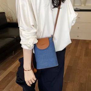 Chic minimalist blue denim crossbody phone bag with brown leather flap worn by model