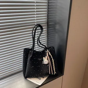 Gros plan d'un sac cabas noir à motif étoilé avec anses tressées et breloque lapin.