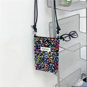 Dettaglio di una mini borsa a tracolla ricoperta di paillettes colorate e label