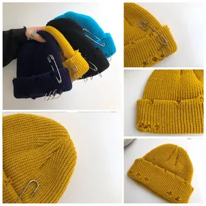 Detail view of distressed knitted beanie with safety pins and rings accessories.