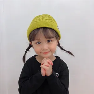 Cute little girl wearing a vibrant mustard green knitted beanie with white side label