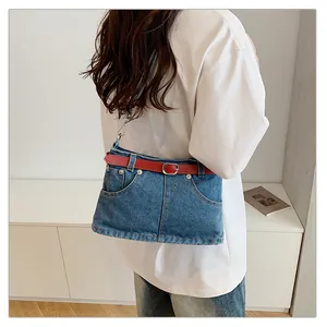 Detail view of niche denim crossbody bag with red belt accent worn by model