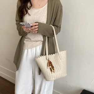 Model holding a stylish beige woven bucket bag with beaded charm and scalloped edges.