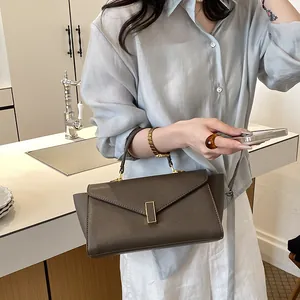 Elegant brown leather top-handle bag featuring a minimalist gold vertical metal clasp.