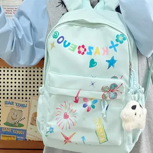 Close-up of mint green backpack with colorful graffiti prints and cute ghost plush charm.