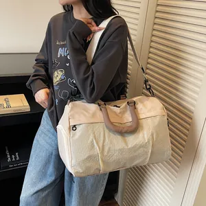 Large beige travel duffel bag with textured panel and brown handles carried by model