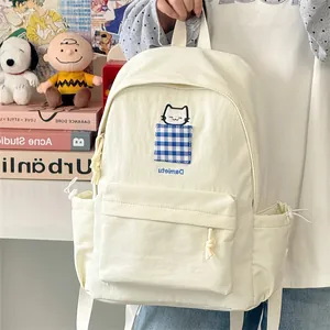 Close-up of minimalist cream backpack with cute cat embroidery and blue gingham pocket
