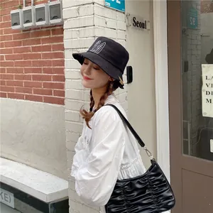 Black bucket hat with white embroidery detail worn by a woman in a street setting