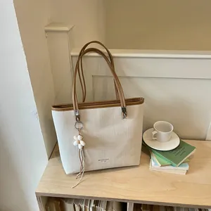 Large beige woven tote bag with brown handles and elegant flower charm detail
