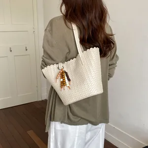Close-up view of a white woven bucket bag with a bead tassel charm styled on a model