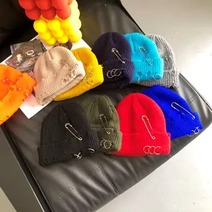 Close-up of distressed knit beanies in multiple colors with ring and pin accents.