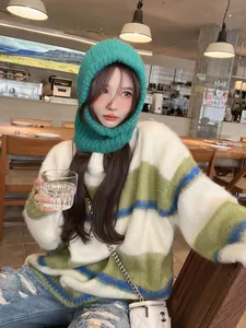 Close-up view of a model wearing a green knitted balaclava in a cozy cafe setting
