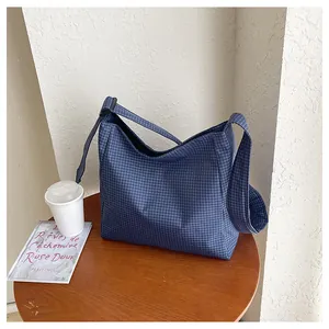Lifestyle detail of a large capacity blue checkered nylon crossbody bag on a wooden table.