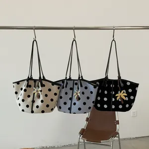 Three stylish polka dot tote bags in beige, blue, and black hanging on a rack