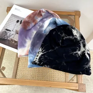 Three stylish tie-dye slouchy beanies in different colors on a wooden table