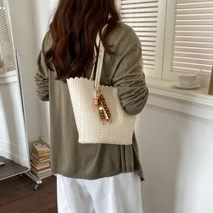 A lifestyle back view of a person carrying a cream woven bucket bag with wood bead charm