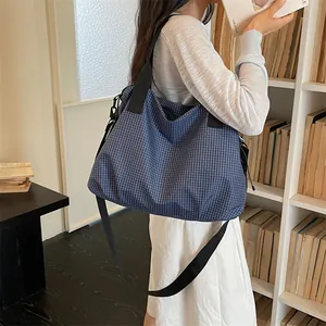 Borsa da viaggio capiente con motivo a quadretti blu portata in un ambiente di biblioteca