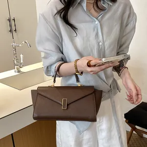 Close-up of a stylish brown leather handbag held by a model in a modern interior.