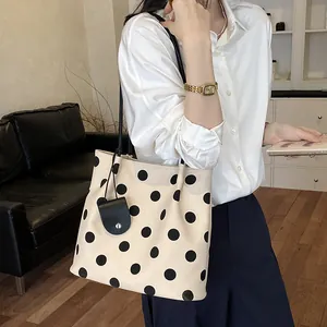 Detailed view of a cream-colored polka dot tote bag styled with a classic white shirt