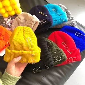 Close-up of distressed knit beanies featuring metal rings and safety pin decorations in many colors.