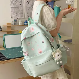 Close-up of mint green backpack with cute animal patterns and plush bow charm.