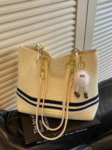 Fashionable woven straw tote bag with navy stripes and a fuzzy monster charm