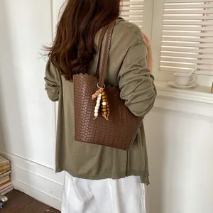 Detailed view of a brown woven bucket bag with beads charm on woman's shoulder.