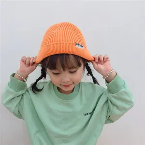 Detailed shot of a child model wearing a bright orange ribbed knitted beanie with a label.