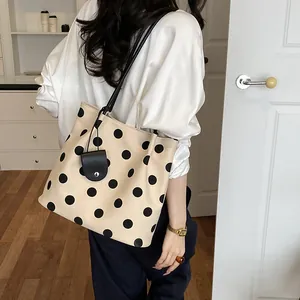 Side view of a vintage cream polka dot tote bag with a small pouch worn by a model