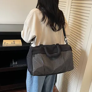 Rear view of a black and grey grid travel bag worn by a model in a modern home setting