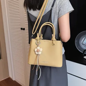 Bolso bombonera amarillo moderno con colgante de flor, usado como bolso bandolera casual.