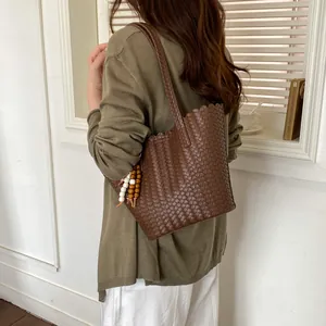 Model in green knit top carrying a stylish brown woven bucket bag with beads charm