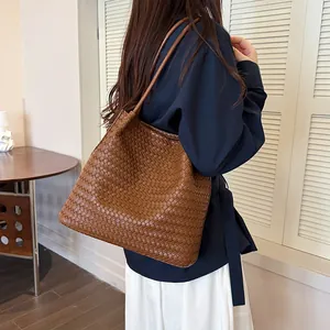 Large brown woven leather tote bag carried by a model showing texture and capacity detail.