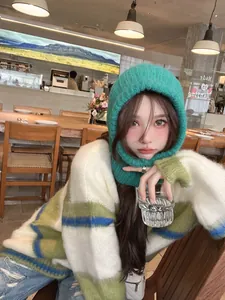 Lifestyle detail of trendy green knitted balaclava hood worn by female model in a cafe setting