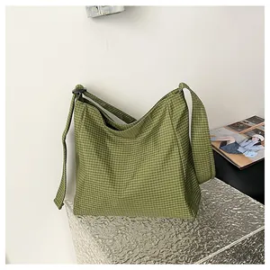 Side view of a green checkered fabric shoulder bag displayed on a silver metallic pedestal