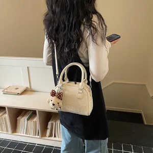 Close-up lifestyle shot of a cream Boston bag with elegant strap and plush charm