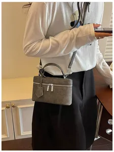 Chic grey box-style crossbody bag with top handle worn by model in a lifestyle setting